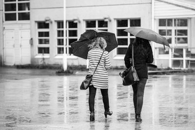 Rear view of women holding umbrellas while walking on walkway during rainy season