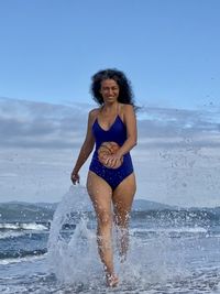 Full length portrait of young woman at beach against sky
