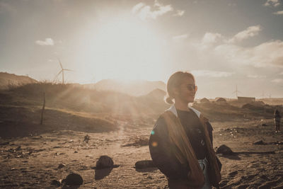 Smiling woman standing on land against windmill during sunny day