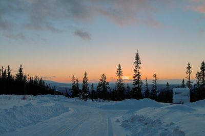 Snow covered landscape against sky at sunset