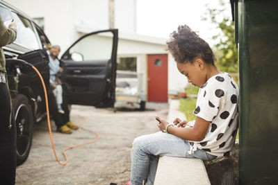 Side view of girl using smart phone while sitting in front yard