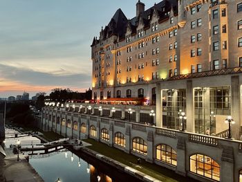 Illuminated buildings by canal against sky at sunset