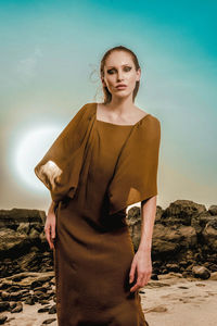 Portrait of young woman standing at beach against sky