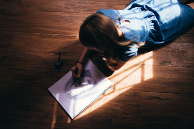 Woman making sketch while lying on hardwood floor