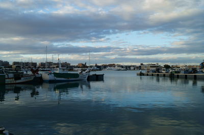 Boats moored at harbor against sky in city