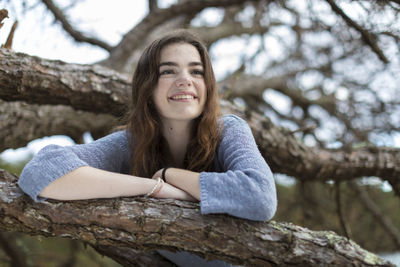 Portrait of smiling young woman sitting on tree trunk