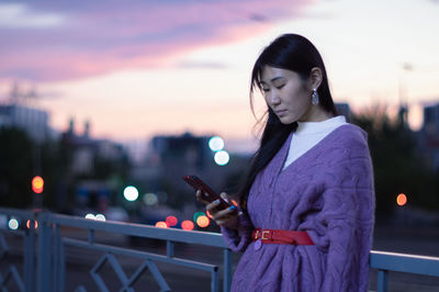 Young woman using phone while standing on railing