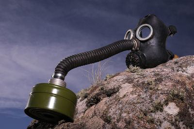 Low angle view of gas mask on rock against sky