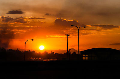 Silhouette street lights against dramatic sky during sunset