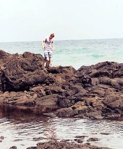 Man standing on rock at beach against sky