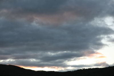 Low angle view of storm clouds over silhouette mountain