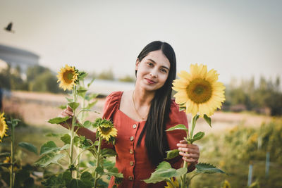 Portrait of smiling young woman with sunflower standing against plants