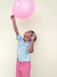 Boy holding pink balloon against wall