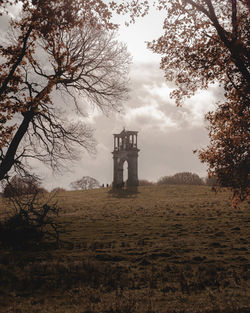 Old tower amidst trees on field against sky