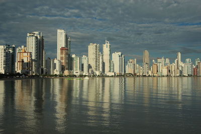 View of city at waterfront against cloudy sky