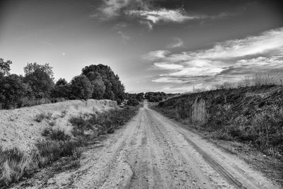 Dirt road amidst field against sky