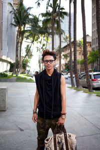 Portrait of young man standing by palm tree in city