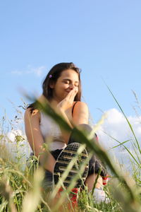 Beautiful young woman lying on field against sky