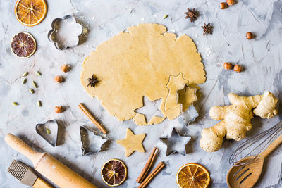 High angle view of dough and cookie cutters with ingredients on marble counter