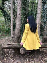 Rear view of woman standing on tree trunk in forest