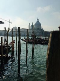 Wooden posts in canal amidst buildings against sky