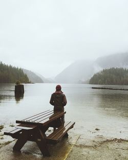 Rear view of man sitting on lake against sky