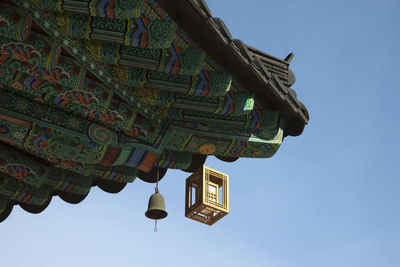 Low angle view of lantern hanging on roof of temple against clear blue sky