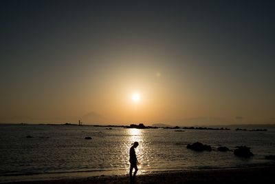 Silhouette person standing on beach against clear sky during sunset