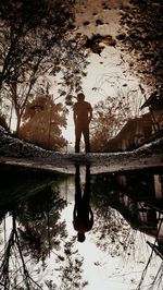 Reflection of silhouette man in lake against sky during sunset