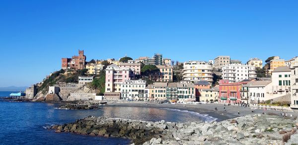 Buildings by sea against clear blue sky