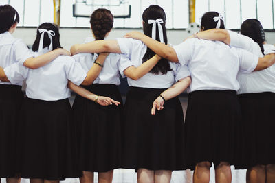 Female friends crossing fingers with arm around standing in school