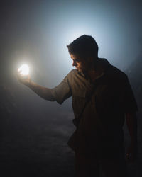 Young male speleologist with bright flashlight in hand exploring dark subterranean cave during extremal adventure