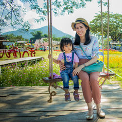 Portrait of smiling mother with daughter sitting on swing in park