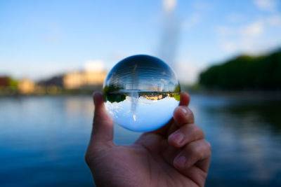 Cropped hand holding crystal ball by lake