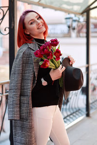 Beautiful young woman standing against red rose