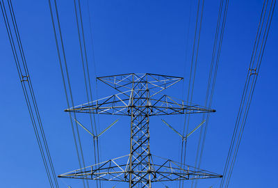 Low angle view of electricity pylon against clear blue sky