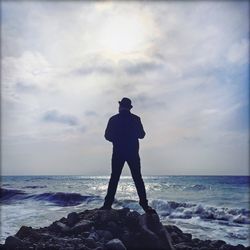 Rear view of man by the sea against cloudy sky