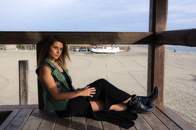 Portrait of woman sitting on pier at beach against sky