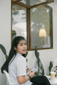 Portrait of young woman using mobile phone while sitting on table at home