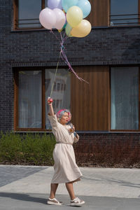 Full length of woman with balloons standing against building