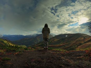 Rear view of young man standing on mountain against cloudy sky