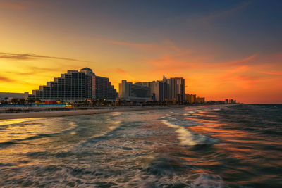 Sea and buildings against sky during sunset