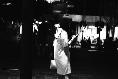 Side view of woman using phone on street in city at night