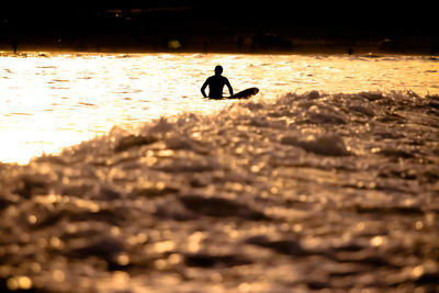 Silhouette man in sea against sky during sunset