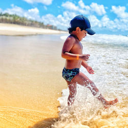 Full length of shirtless boy splashing water on beach