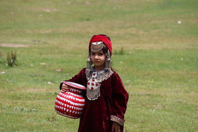 Portrait of girl in traditional clothing holding container while standing on field