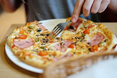 Midsection of person cutting pizza using fork in restaurant