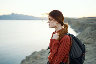 Side view of young woman standing by sea against sky