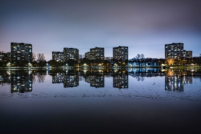 Illuminated buildings by river against sky at night