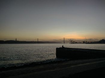 Suspension bridge over sea against sky during sunset